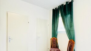 Ein Zimmer mit Glastisch, zwei Holzsesseln, einer weißen Tür und grünen Vorhängen.