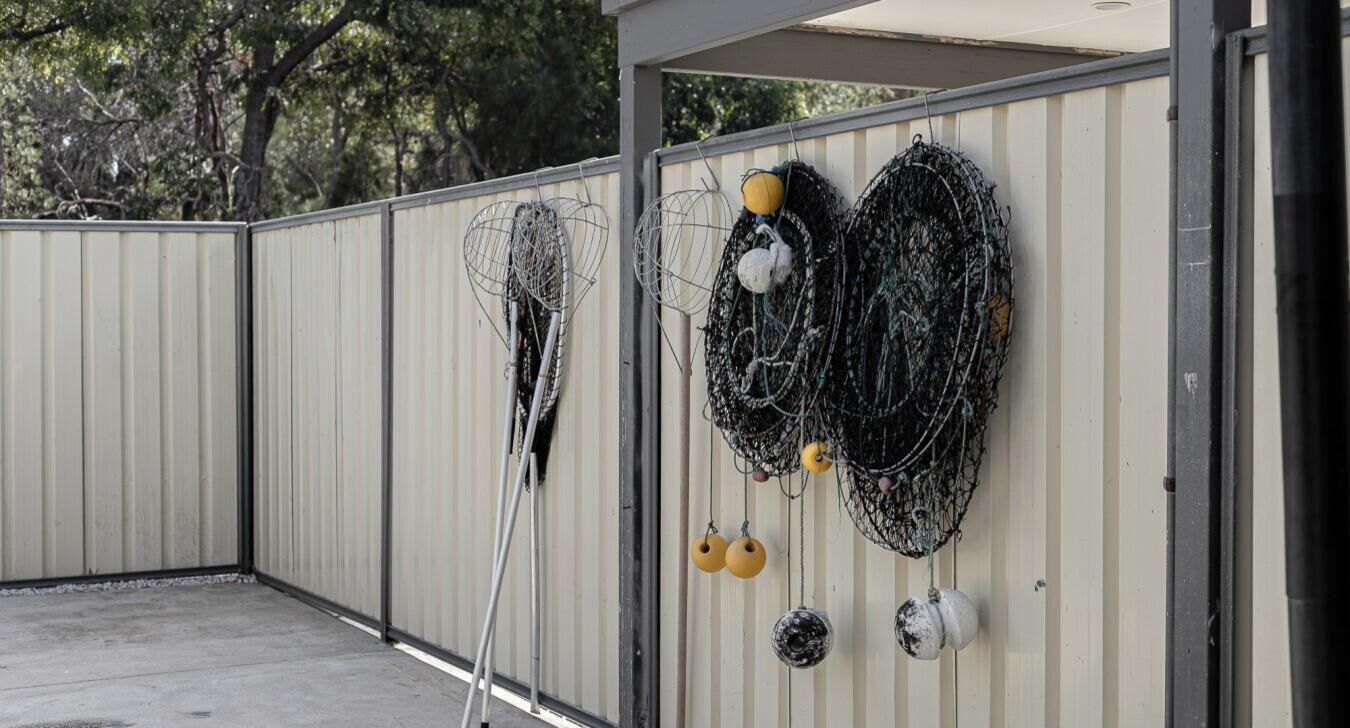 A metal fence with a concrete floor, a metal structure, and some fishing nets and buoys.