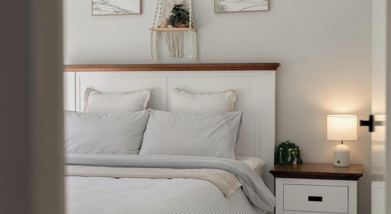A neatly made bed with striped bedding, a wooden headboard, a bedside table with a lamp, and wall art above the bed.