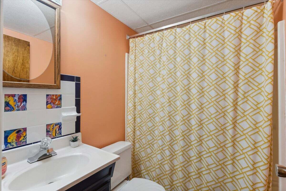 Ein Badezimmer mit einem weißen Waschbecken, einem Spiegel, einer Toilette und einem duschvorhang mit Muster.