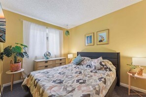 A bedroom with a bed, bedside tables, a window with curtains, and wall art.