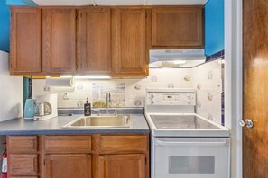 A compact kitchen with wooden cabinets, a sink, a stove, and a coffee maker.