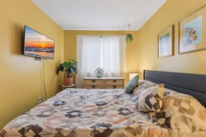 Un dormitorio con una cama, televisión, ventana con cortinas y una planta.