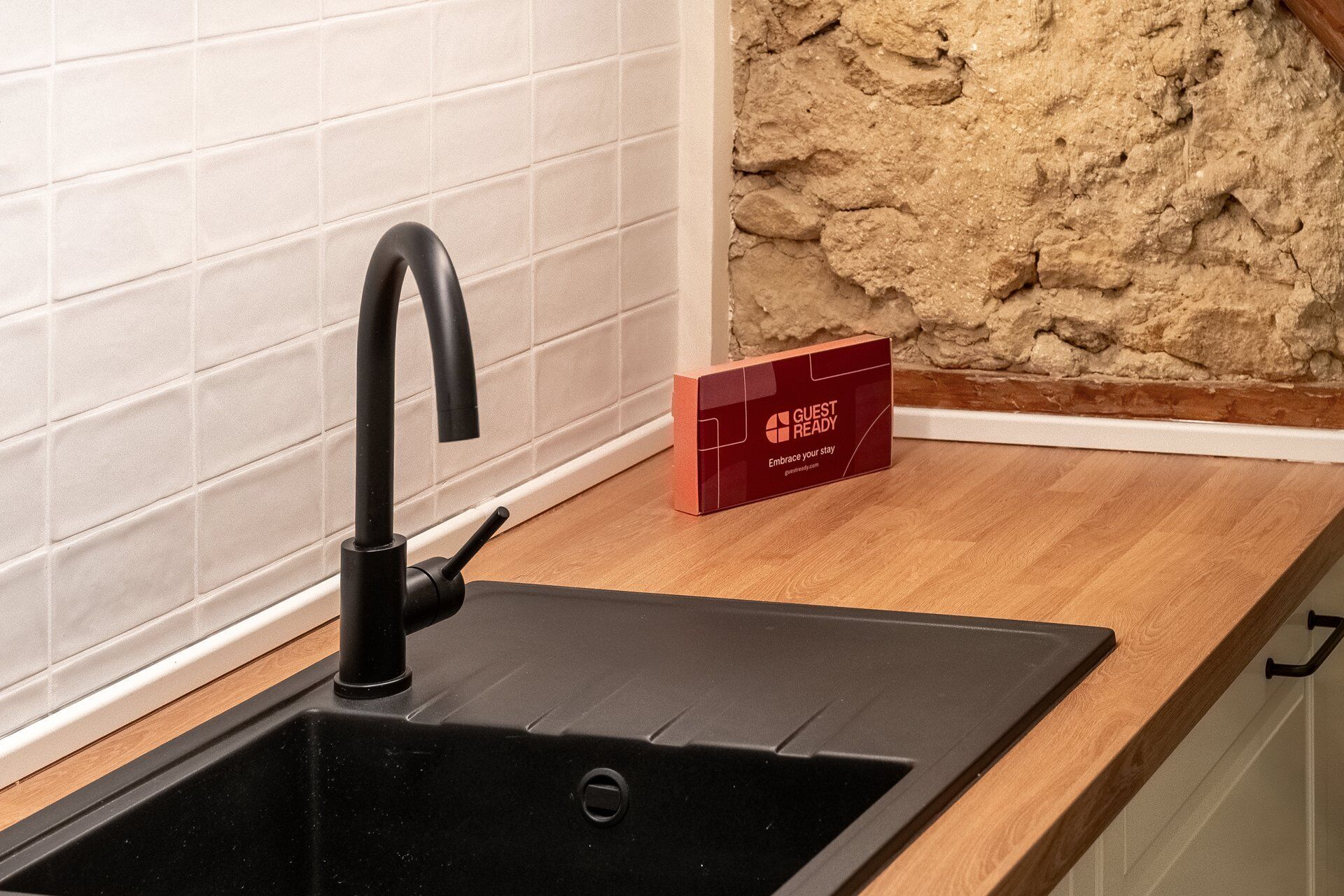 Een zwarte spoelbak met een moderne kraan, een houten aanrechtblad en een stenen muur op de achtergrond.