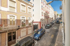 Eine schmale Kopfsteinpflasterstraße, gesäumt von historischen Gebäuden, parkenden Autos und einem strahlend blauen Himmel.
