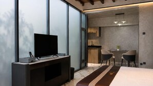 Una habitación de hotel moderna con una cama grande, un televisor sobre un mueble bajo, una pequeña cocina y un espacio para sentarse.