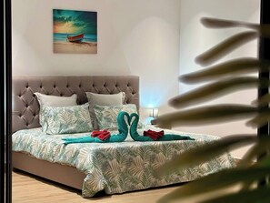 Une chambre à coucher avec une tête de lit capitonnée, un lit recouvert d’une couvre-lit à motifs de feuilles, des oreillers et un tableau représentant un bateau accroché au mur.