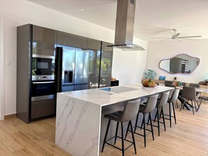 Une cuisine moderne dotée d’un îlot central, de tabourets de bar, d’un coin repas et d’un ventilateur de plafond.