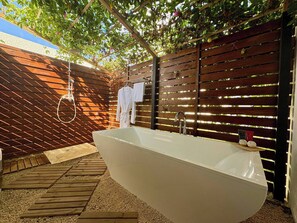 Une salle de bain extérieure moderne avec une baignoire sur pieds, une terrasse en bois et une clôture en bois à lattes verticales.