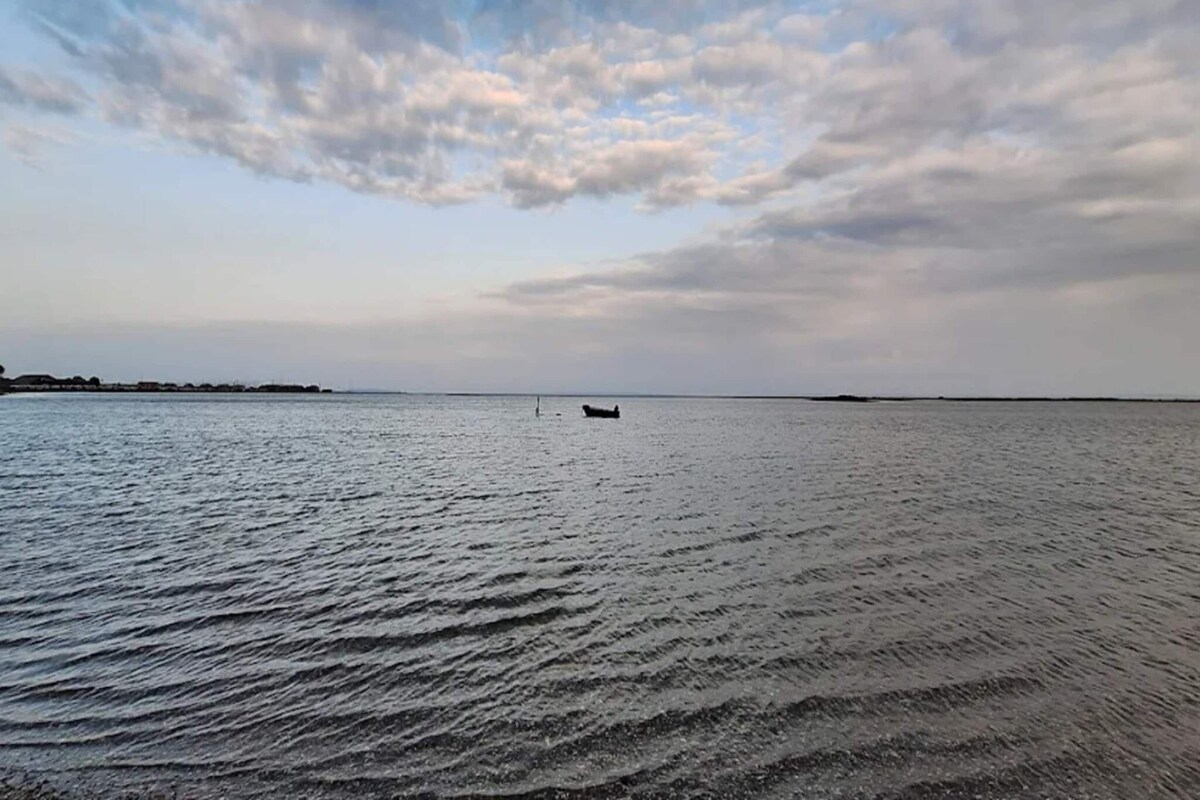 A calm body of water with a boat in the distance and a cloudy sky above.