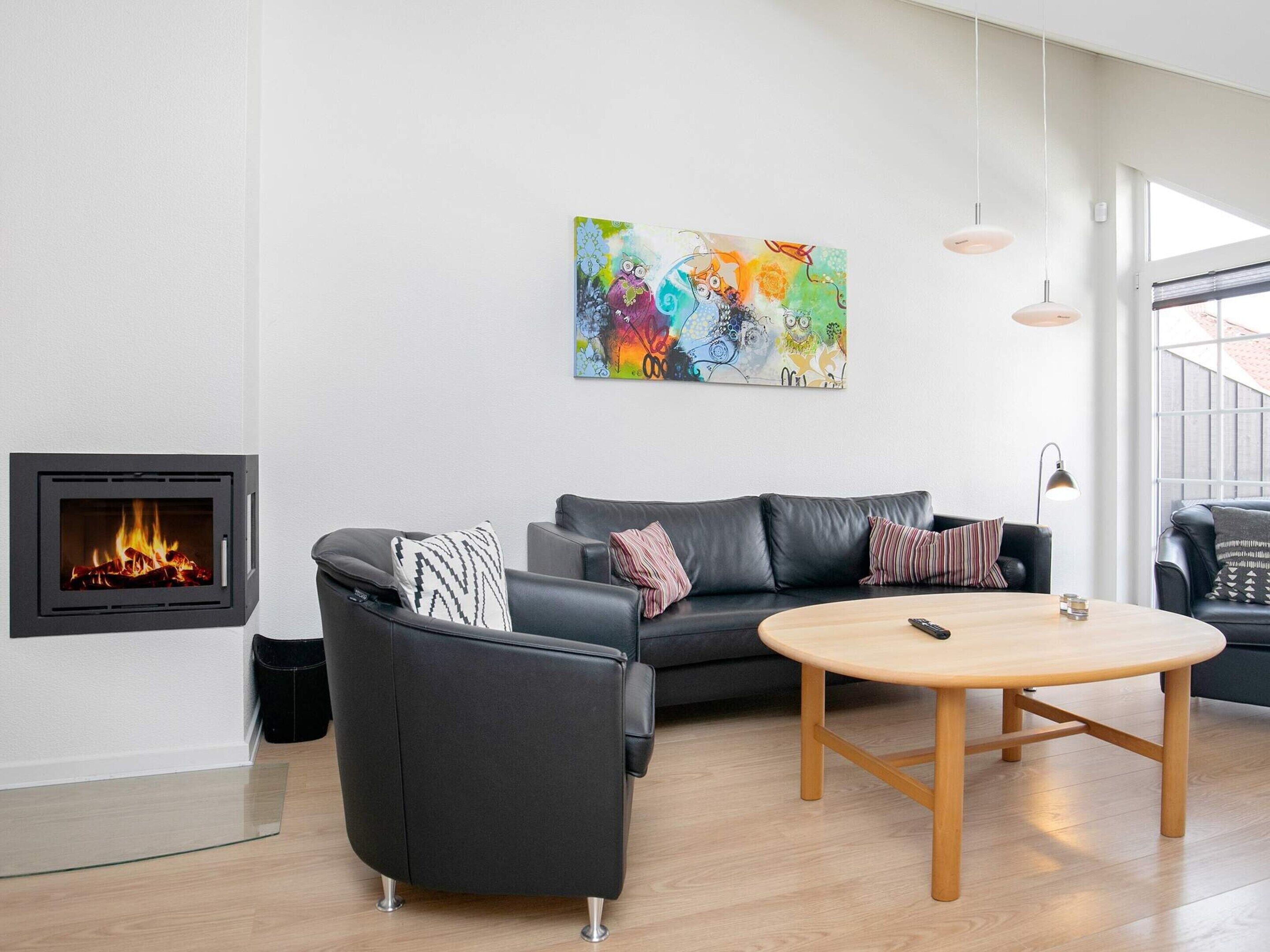 Ein modernes Wohnzimmer mit Kamin, einer schwarzen Ledersofa, einem runden Holztisch und einem farbenfrohen abstrakten Gemälde an der Wand.