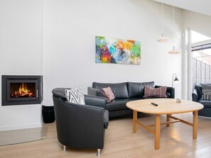 Ein modernes Wohnzimmer mit Kamin, einer schwarzen Ledersofa, einem runden Holztisch und einem farbenfrohen abstrakten Gemälde an der Wand.