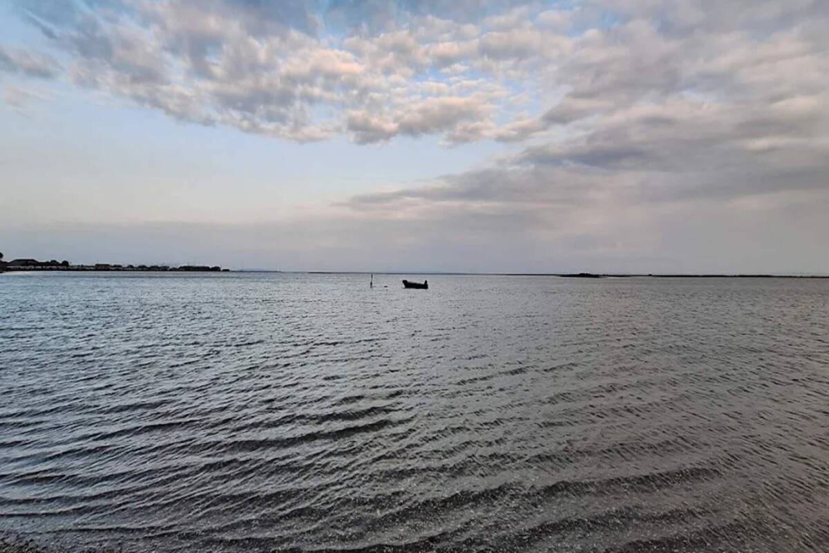 Ruhige Wasserfläche mit einem Boot in der Ferne und bewölktem Himmel.
