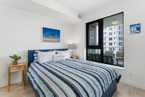 Ein modernes Schlafzimmer mit einem großen Bett, einem Nachttisch, einer Topfpflanze, einem Fenster mit Stadtblick und einem Bild an der Wand.