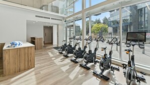 A gym with stationary bikes, a reception desk, and large windows. - Epic Lake Views | Modern 1BR (Kelowna)