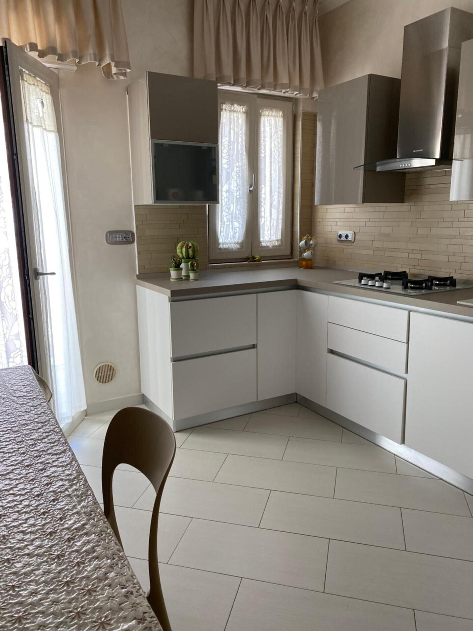 A modern kitchen with white cabinets, a gas stove, and a window with curtains.