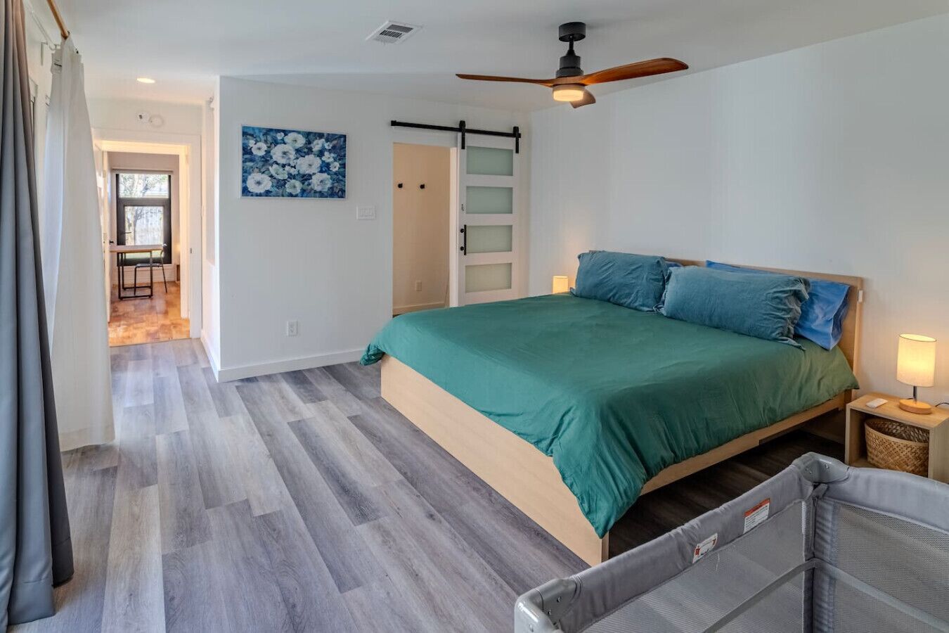 A bedroom with a bed, a ceiling fan, a door, and a painting on the wall.