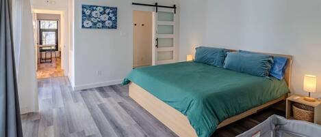 A bedroom with a bed, a ceiling fan, a door, and a painting on the wall.