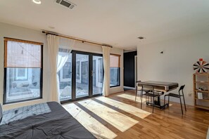 A room with a bed, a dining table with chairs, a bookshelf, and large windows with curtains. - Charming Houston Getaway (Houston)