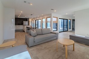 A modern living room with a sofa, two small tables, and a kitchen in the background. - Charming Houston Getaway (Houston)
