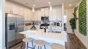 A modern kitchen with white cabinets, stainless steel appliances, a central island with stools, and a wall-mounted plant. - Cozy 3BR Richmond perfect for relaxation (Richmond)