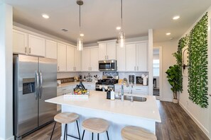 A modern kitchen with white cabinets, stainless steel appliances, a central island with stools, and a wall-mounted plant. - Cozy 3BR Richmond perfect for relaxation (Richmond)
