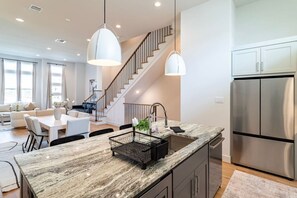 A modern kitchen with a marble countertop, stainless steel appliances, and a staircase leading to a living area. - Downtown home near stadiums and convention center (Houston)