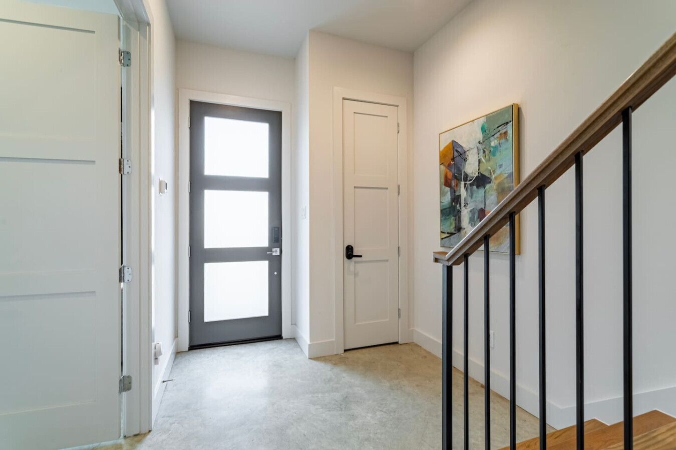 Un couloir avec une porte, un escalier et un tableau accroché au mur.