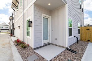 A residential building with a front porch, a door, and a small garden area with flowers. - Modern Maroon 3BR Home near Houston Downtown (Houston)