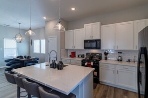 A modern kitchen with white cabinets, a central island, a microwave, a stove, and pendant lighting. - Modern Maroon 3BR Home near Houston Downtown (Houston)