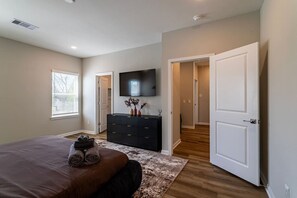 A bedroom with a bed, dresser, TV, and a hallway leading to another room. - Modern Maroon 3BR Home near Houston Downtown (Houston)