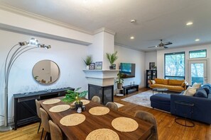 Ein modernes Wohnzimmer mit Kamin, Fernseher, einer Couch und einem Essbereich mit Holztisch und Stühlen.