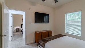 Ein Schlafzimmer mit einem Bett, einem Schminktisch, einem Fernseher, einem Deckenventilator und einem Fenster.
