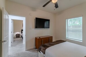 Ein Schlafzimmer mit einem Bett, einem Schminktisch, einem Fernseher, einem Deckenventilator und einem Fenster.