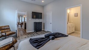 Ein Schlafzimmer mit Bett, einem an der Wand befestigten Fernseher, einem Schminktisch und einer Tür zu einem Badezimmer.