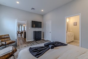 Ein Schlafzimmer mit Bett, einem an der Wand befestigten Fernseher, einem Schminktisch und einer Tür zu einem Badezimmer.