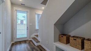 Ein Korridor mit Holzboden, weißen Wänden, einer Tür mit Rollläden und einer Treppe mit weißer Geländer.