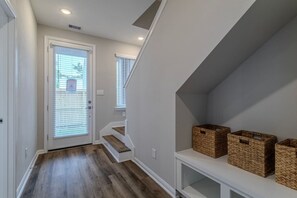 Ein Korridor mit Holzboden, weißen Wänden, einer Tür mit Rollläden und einer Treppe mit weißer Geländer.