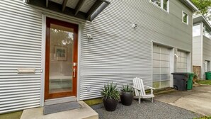 A residential building with a metal siding exterior, a wooden front door, a garage door, and two potted plants. - Home for 4 near i10 / Memorial / Bayou Trails (Houston)