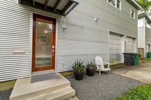 A residential building with a metal siding exterior, a wooden front door, a garage door, and two potted plants. - Home for 4 near i10 / Memorial / Bayou Trails (Houston)