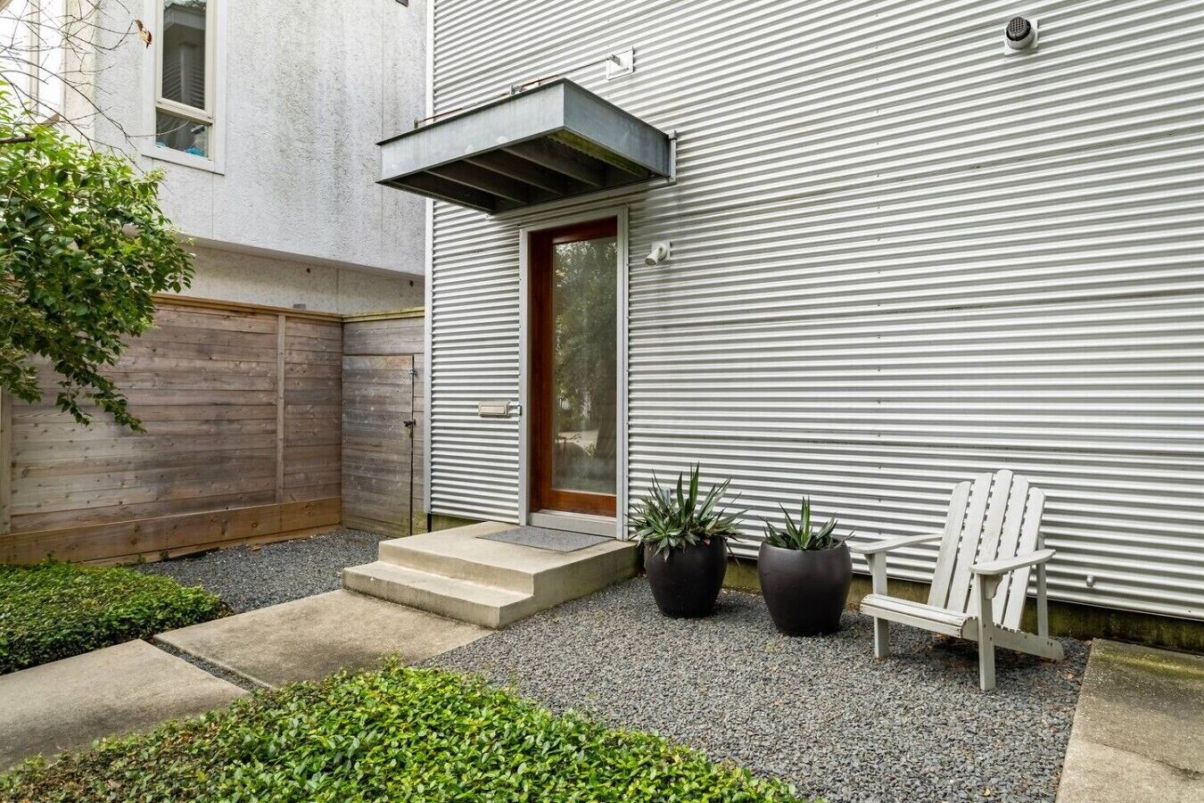 A modern building with a metal exterior, a wooden fence, a door, and two potted plants.