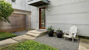 A modern building with a metal exterior, a wooden fence, a door, and two potted plants. - Home for 4 near i10 / Memorial / Bayou Trails (Houston)