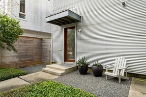 A modern building with a metal exterior, a wooden fence, a door, and two potted plants. - Home for 4 near i10 / Memorial / Bayou Trails (Houston)