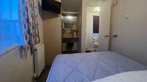 Quarto de hotel com cama, televisão, banheiro com espelho e radiador.