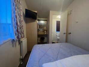 A hotel room with a bed, a television, a bathroom with a mirror, and a radiator. - Lyons Robin Hood - Holiday Accommodation 17224 (Rhyl)
