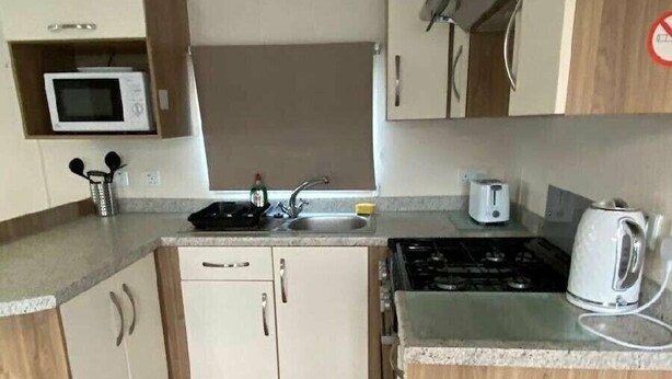 Uma cozinha compacta com micro-ondas, fogão, pia e lixeira.