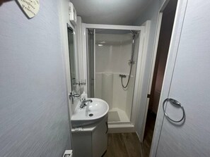 A small bathroom with a sink, mirror, and glass-enclosed shower. - Lyons Robin Hood - Holiday Accommodation 17224 (Rhyl)