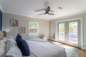 Ein Schlafzimmer mit Bett, Deckenventilator, Fenster und Spiegel, sowie einer Schiebeglastür zu einem Außenbereich.