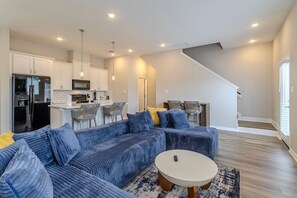 Ein modernes Wohnzimmer mit einem Ecksofa, einem runden Couchtisch und einer Küchenzeile mit weißen Schränken und einem schwarzen Kühlschrank.