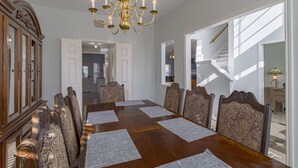 Un comedor con una mesa de madera, seis sillas, una lámpara de araña y vistas a una escalera.